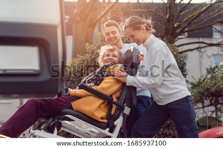 Two helpers picking up disabled senior woman in wheelchair for transport Royalty-Free Stock Photo #1685937100