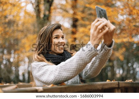 Beautiful young happy woman taking selfie with smartphone in autumn park. Season, technology and people concept .
