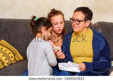 Grandma Looking At Old Photos With Grandchildren To Refresh Memory. Happy Family, Cozy Home Moments.
