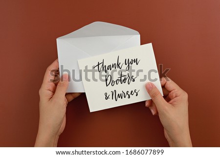 Female hand holding card with words Thank You Doctors & Nurses.