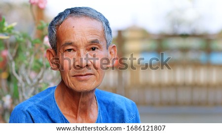portrait of happy and unsmiling Thai countryside senior asian man with delicate facial features  looking at camera while standing outside in front of his home in the garden .A male older than 60. Royalty-Free Stock Photo #1686121807