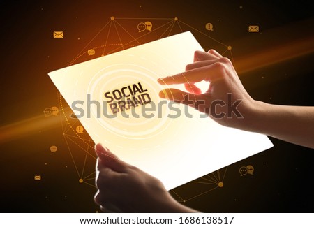 Holding futuristic tablet with SOCIAL BRAND inscription, social media concept