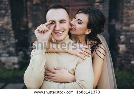 Cheerful bride bites the groom with a ring instead of glasses for the ear. Wedding portrait of smiling newlyweds. Funny picture, concept.