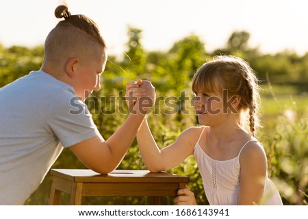 Boy and girl friends or brother and sister in nature. Arm Wrestling. Fun games for the summer holiday, gender opposition, competition, struggle.