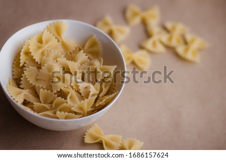 Farfalle pasta in a white ceramic bowl against a background of craft paper: stocks during an epidemic, dry ingredients for cooking