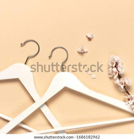 Creative spring sale concept. White wooden hangers with spring sprigs of apricot flowers on beige background top view flat lay. Fashion spring discounts shopping sale store promo design minimalism