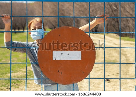 Caucasian women standing in protective mask behind closed gate with red stop sign. in quarantine for coronavirus covid-19. Stay at home concept