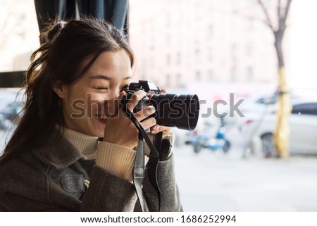 Young pretty woman taking pictures via modern camera while sitting in cafe	