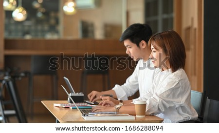 Photo of website administrator team working with computer tablet and laptop while sitting together at the modern wooden table over luxury cafe as background. Working outside the office concept.