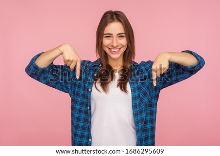 Look down, choose option below! Portrait of charming brunette girl in checkered shirt pointing down at place for advertisement, commercial content. indoor studio shot isolated on pink background Royalty-Free Stock Photo #1686295609