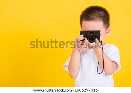 Asian Thai happy portrait cute little cheerful child boy photographer he's holding photo camera compact doing taking the picture, studio shot isolated on yellow background with copy space