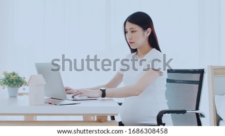 Asian pregnant women sit and work from home with happiness. By using the laptop to operate Planning meetings with business people from various locations. Or order online Concept social distancing