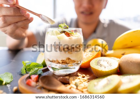 A blur man background scooping a glass of yogurt mixed with cereal Green apples, strawberry, almonds and mint leaves by a wooden spoon. Conceptual of healthy food for good life with copy space.