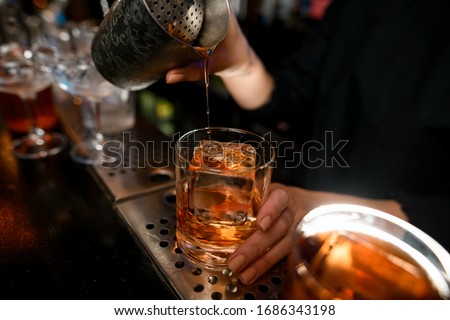 Close-up bartender masterfully pours old fashioned cocktail into glass with large piece of ice on the bar counter. Royalty-Free Stock Photo #1686343198