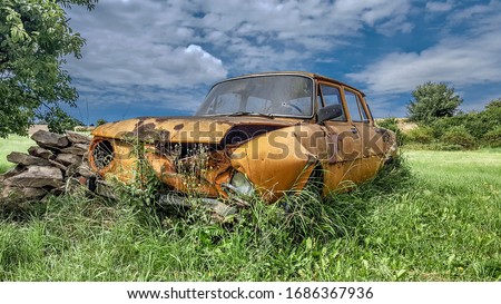 Old Rusty squalid destroyed Car wrack vehicle with shot hole in the front glass windshield windscreen covered by grass in a czech field lost nature  Royalty-Free Stock Photo #1686367936
