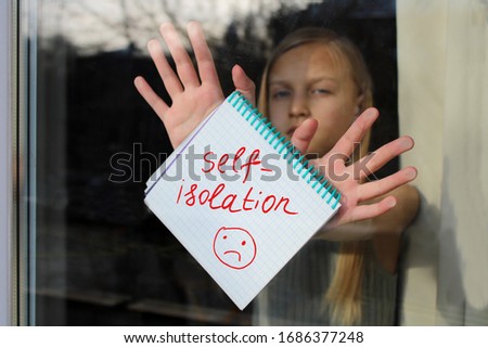 A notebook with the inscription Self Isolation in the hands of a girl behind the glass of the apartment. Quarantine or self-isolation due to the pandemic of Covid-19. Self-isolation sign. Stay at home Royalty-Free Stock Photo #1686377248