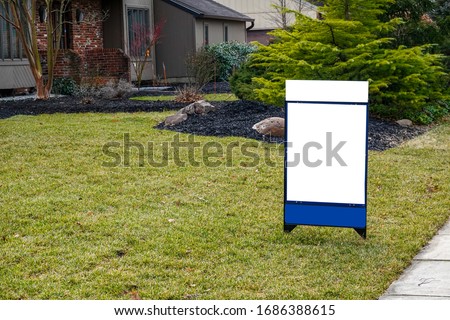 Blank white lawn sign in the grass in front of a house.