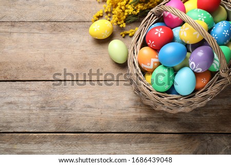 Colorful Easter eggs and mimosa flowers on wooden background, flat lay. Space for text