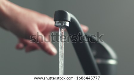 Woan is opening and closing water flow tap and filling sink with water. Water running from chrome faucet. Bathroom plumbing. Using water resources. Royalty-Free Stock Photo #1686445777