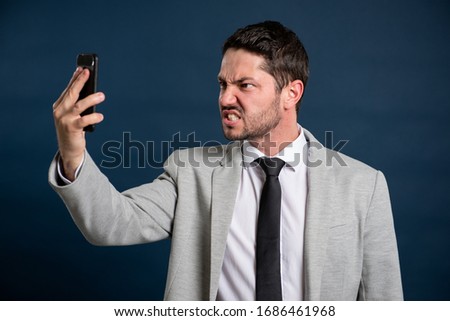 Portrait of business young male looking mad at telephone on blue background with copy space advertising area