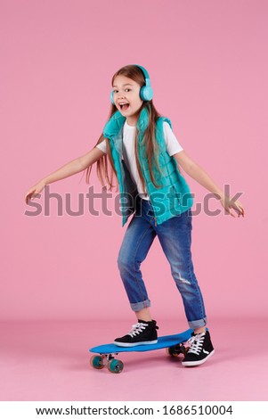 Beautiful little blonde kid girl 7-10 years old in jacket posing isolated on pastel pink background children portrait. Childhood lifestyle concept. Mock up copy space. Hold blue skateboard