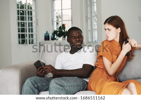Beautiful young couple at home on the couch communicating with the phone in their hands