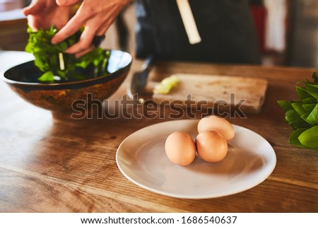 Green leafs of salate and chiken eggs one the wooden brown table
