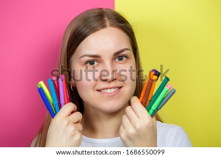 Beautiful young girl in a white T-shirt holds multicolored felt-tip pens for drawing