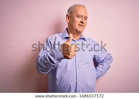 Middle age handsome hoary man wearing casual shirt standing over pink background doing happy thumbs up gesture with hand. Approving expression looking at the camera showing success.