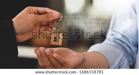 Cropped image Hands of real estate agent offering/giving a house key to smart man in blue shirt while standing together over modern bank as background. Broker/Seller/Dealer concept. Royalty-Free Stock Photo #1686558781