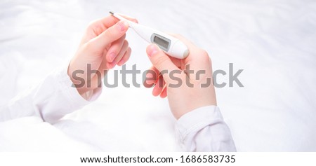 A young woman has the flu at home. In the woman's hands lies an electronic thermometer with a temperature reading after the measurement. Flu and colds, viral diseases. Concept