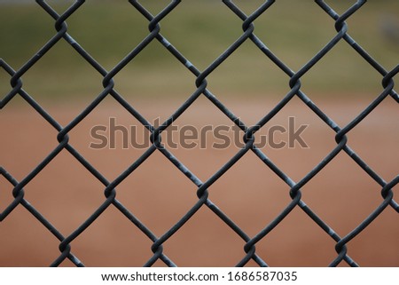Close-up of a chain link fence with a blurred baseball field and grass behind it.