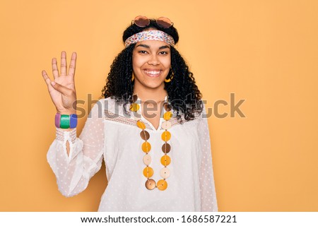 Young african american curly hippie woman wearing sunglasses and vintage accessories showing and pointing up with fingers number four while smiling confident and happy.