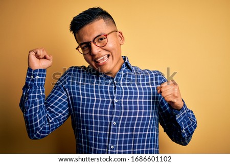 Young handsome latin man wearing casual shirt and glasses over yellow background Dancing happy and cheerful, smiling moving casual and confident listening to music