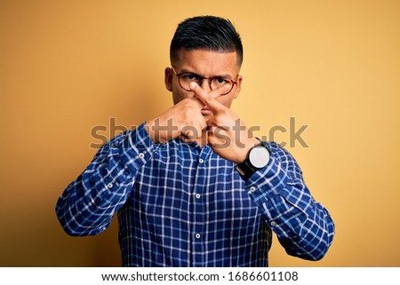 Young handsome latin man wearing casual shirt and glasses over yellow background Rejection expression crossing fingers doing negative sign