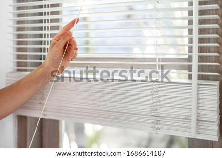 Concept of lighting range control. Cropped view of woman pull rope, closed modern white jalousie on windows in bright room Royalty-Free Stock Photo #1686614107