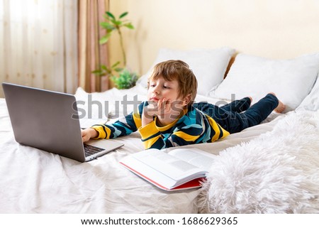 Distance learning online education. Caucasian happy boy with book studying at home with digital tablet laptop notebook and doing school homework. Sitting on bed with training books.