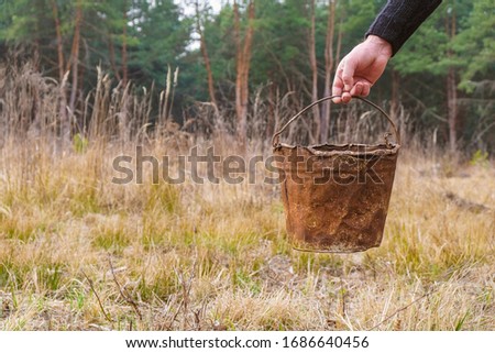 Rusty bucket in human hand on forest background. Trash in the forest. Environmental disaster. Royalty-Free Stock Photo #1686640456