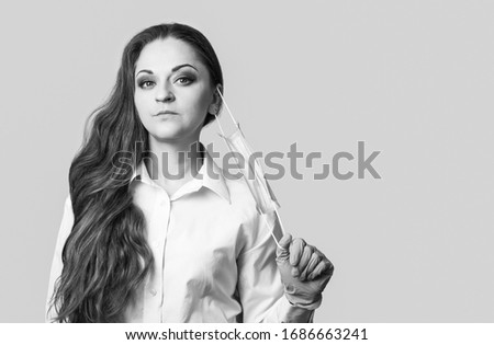 Woman straightens medical mask on her face, she is in gloves isolated on grey background. Black and white photography with place for text