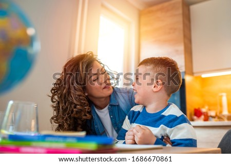 Kind mother helping her son doing homework in kitchen. Children's creativity. Portrait of smiling mother helping son with homework in kitchen at home