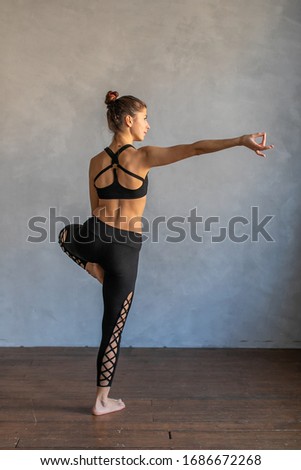 Young woman standing in a yoga exercise position. Girl balancing, practice stretch exercise at yoga class - she is standing on one leg