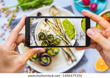Phone picture of food. Hands make smartphone photography of eggplants for social media blogging. Concept for online order services. Vegan meal.