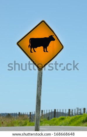 A yellow warning sign alerts motorists to free ranging cattle crossing on empty road. No people. Copy space