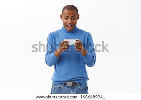 Internet, online lifestyle and people concept. Portrait of excited, happy young african american adult guy playing racing game, watching movie or video on smartphone, hold mobile phone both hands