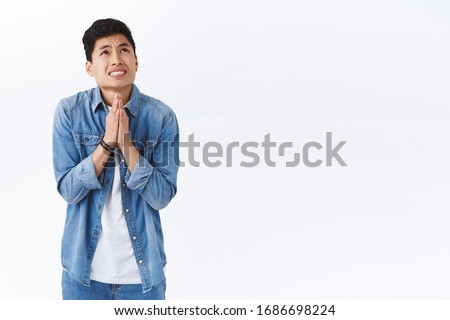 Portrait of intense young worried asian man nervously praying for dream come true, talking to God, press hands together in pray raising head in the sky to plead, begging, standing white background Royalty-Free Stock Photo #1686698224