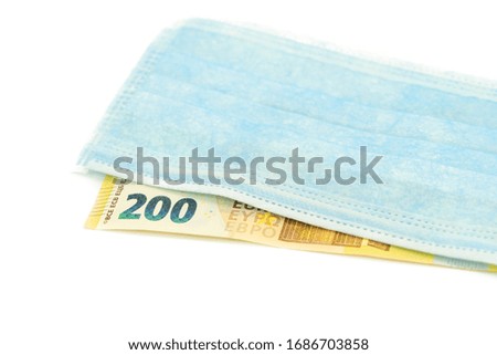 A blue medical mask lies on a banknote of 200 euros. Concept of buying a mask in Europe, protection against the virus. Isolated white background.
