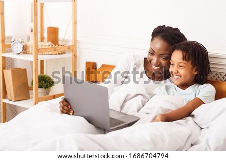 Things To Do At Home With Family. Black mom and daughter using laptop, lying in bed together. Free space