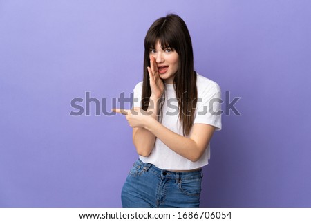 Young Ukrainian woman isolated on purple background pointing to the side to present a product and whispering something