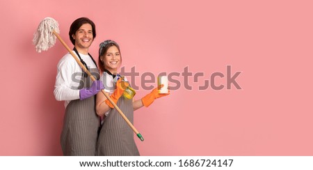 Janitors Team. Happy Man And Woman In Aprons With Cleaning Supplies In Hands Posing Over Pink Background, Panorama With Copy Space