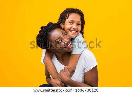Togetherness Concept. African daughter hugging her mum from the back, showing her love, yellow studio wall Royalty-Free Stock Photo #1686730120